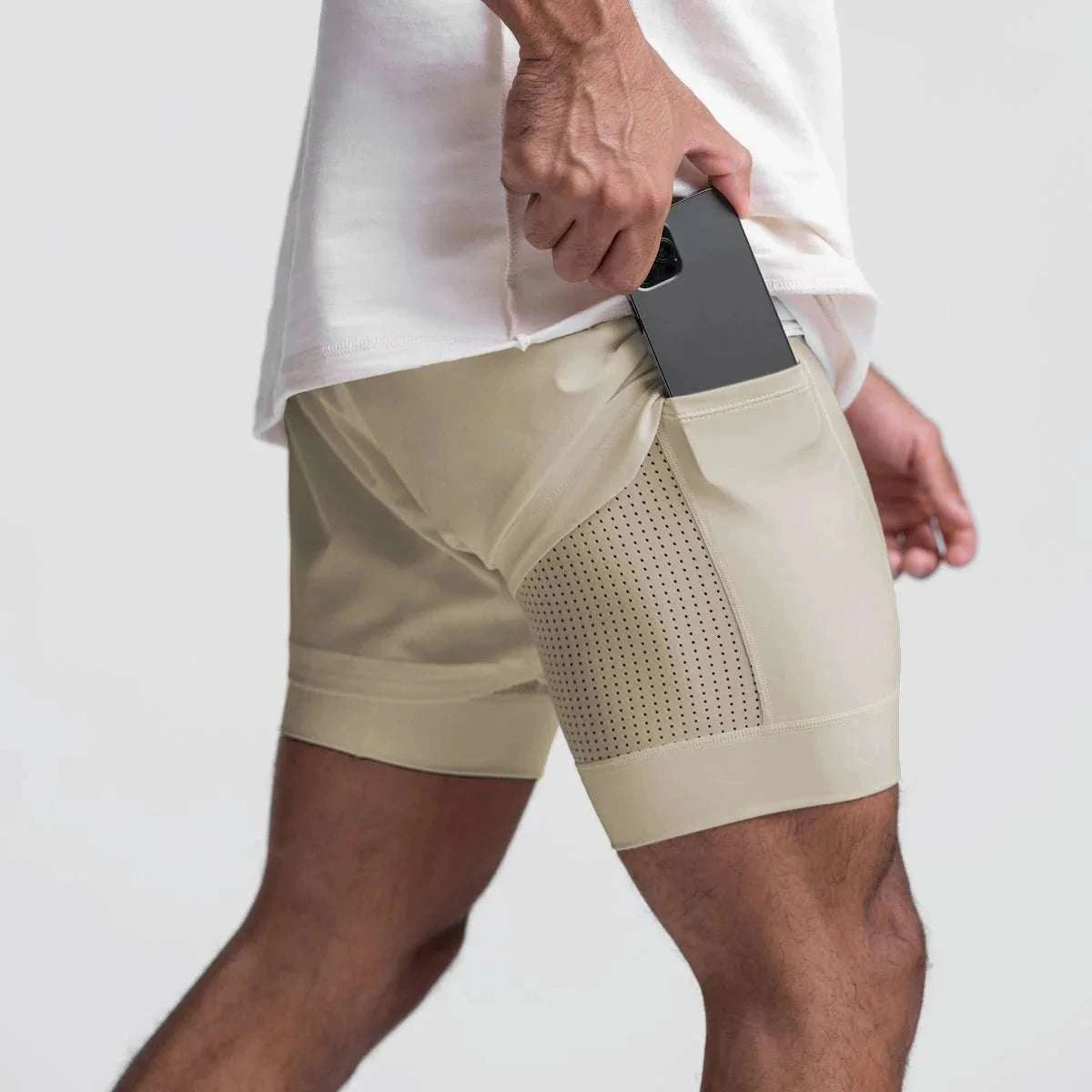 Men wearing beige 2 in 1 fitness gym shorts with breathable mesh and phone pocket inserting a phone.