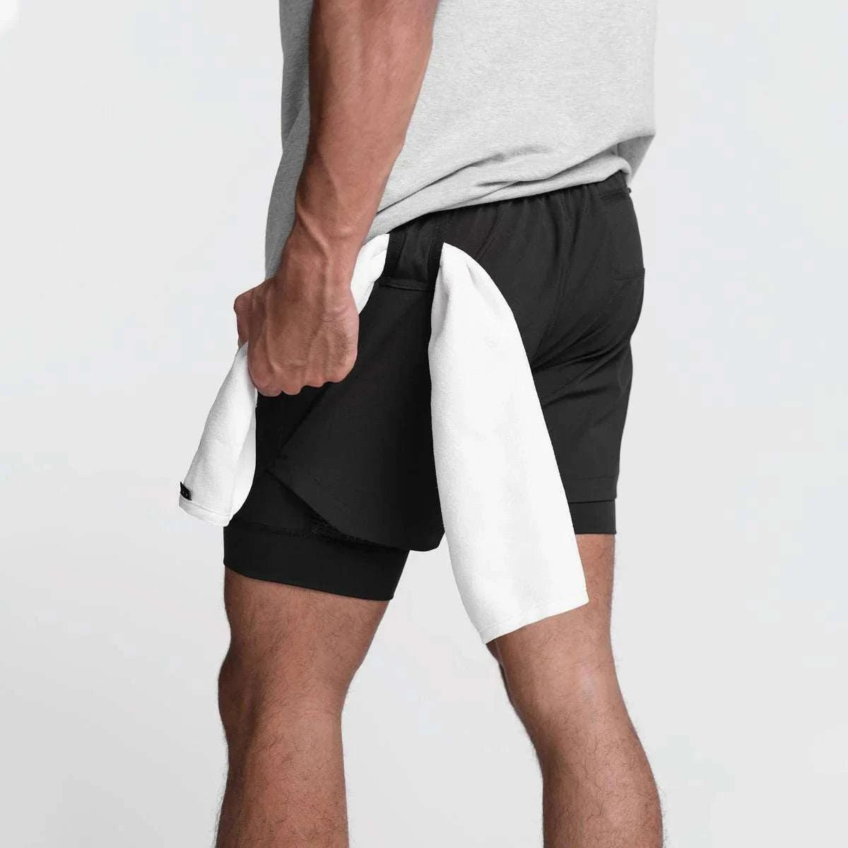 Men wearing black 2 in 1 fitness gym shorts with towel loop holding a white towel.