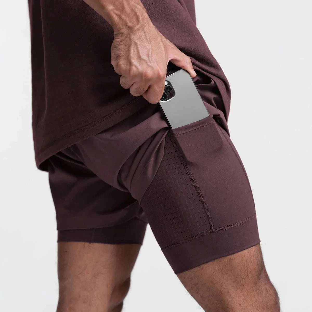Men wearing 2 in 1 fitness gym shorts with breathable mesh and phone pocket inserting smartphone