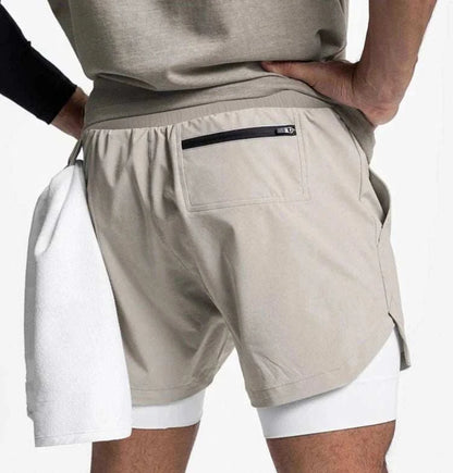 Men wearing beige 2 in 1 fitness gym shorts with breathable inner tights and a towel loop carrying a white towel.