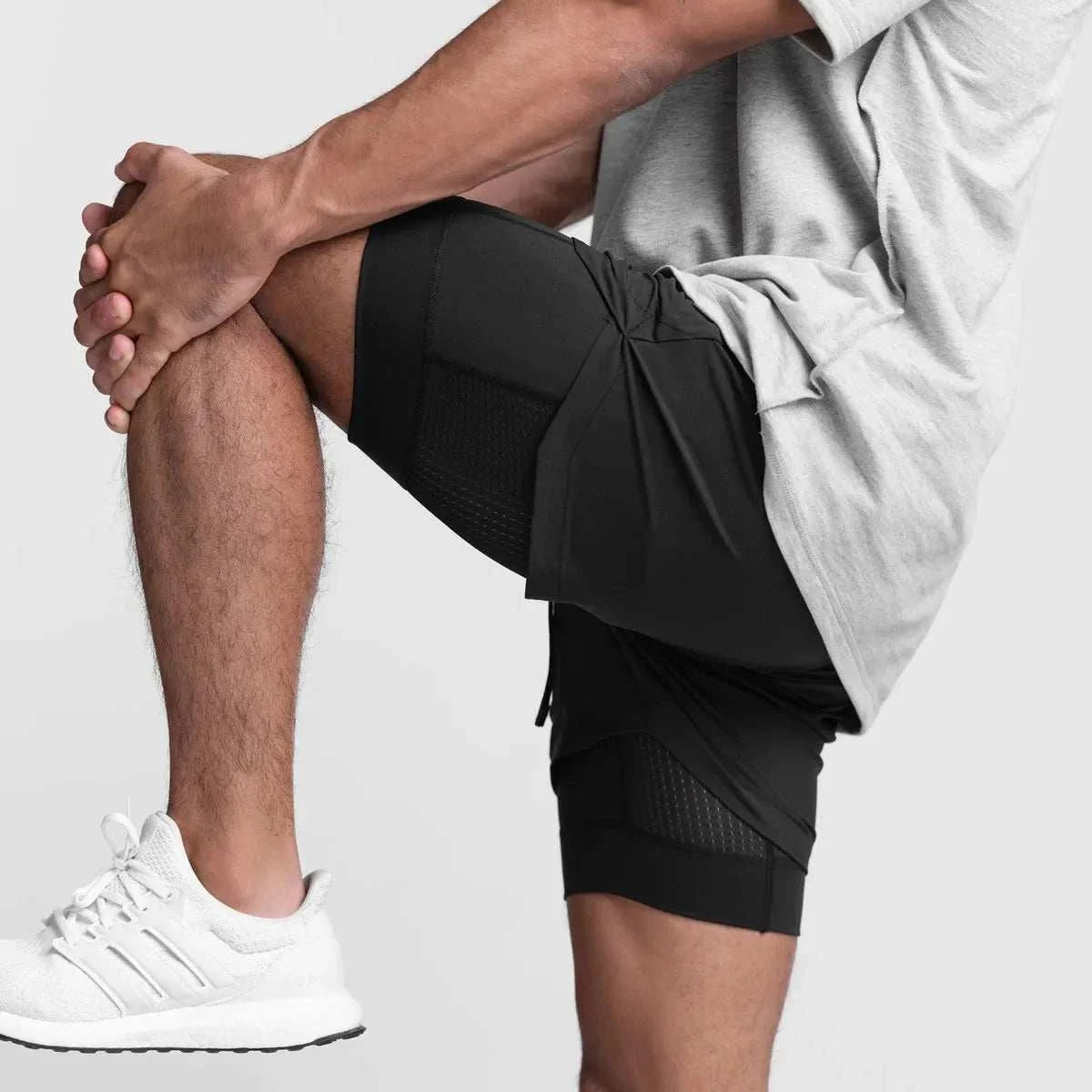 Men wearing black 2 in 1 fitness gym shorts with breathable mesh inner tights stretching leg