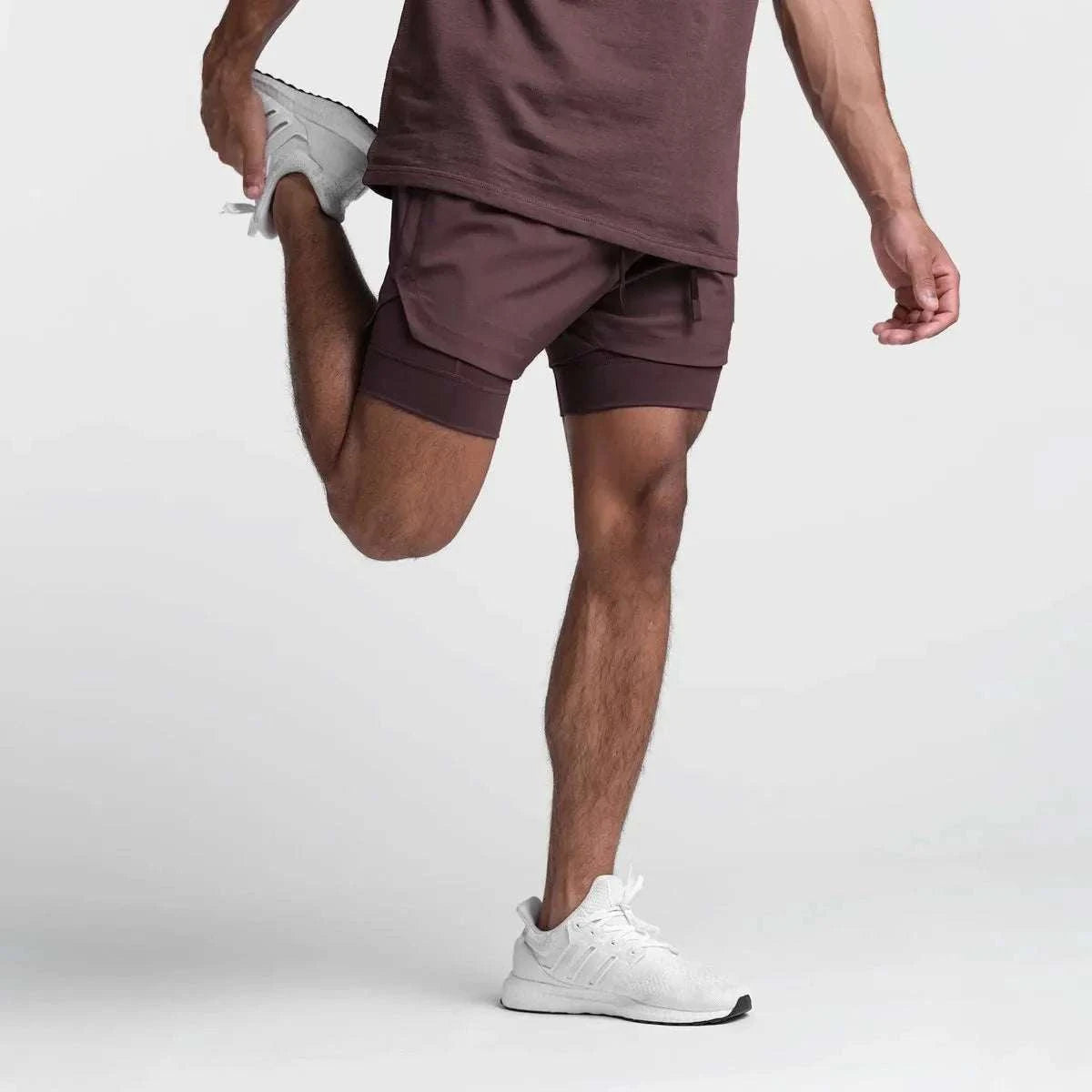 Men wearing maroon 2 in 1 fitness gym shorts with towel loop stretching leg in white sneakers